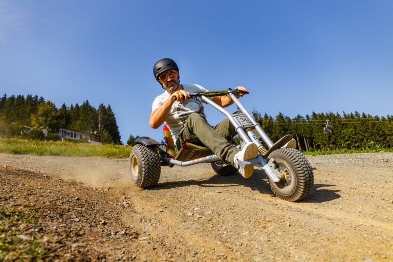 Mann fährt lächelnd im Sommer einen Abhang mit einem Mountaincart hinunter