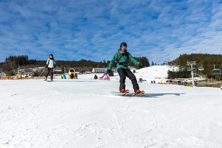 Skifahrer und Snowboarder fahren einen verschneiten Hang bei blauem Himmel herunter