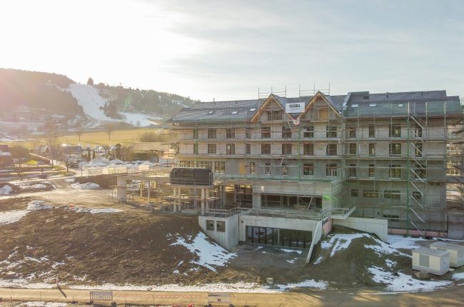 Au&szlig;enansicht des Hotels Schutzh&uuml;tte im Sonnenuntergang vor einer Skipiste