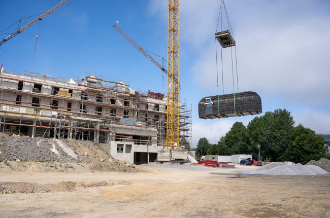 Schwarze Iglusauna wird per Kran in Richtung eines Rohbaus gehoben